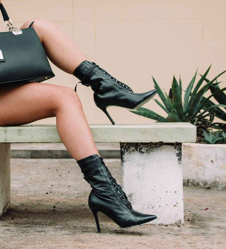 woman wearing black and white polka dot shirt with black short shorts holding black leather tote bag sitting on white concrete bench